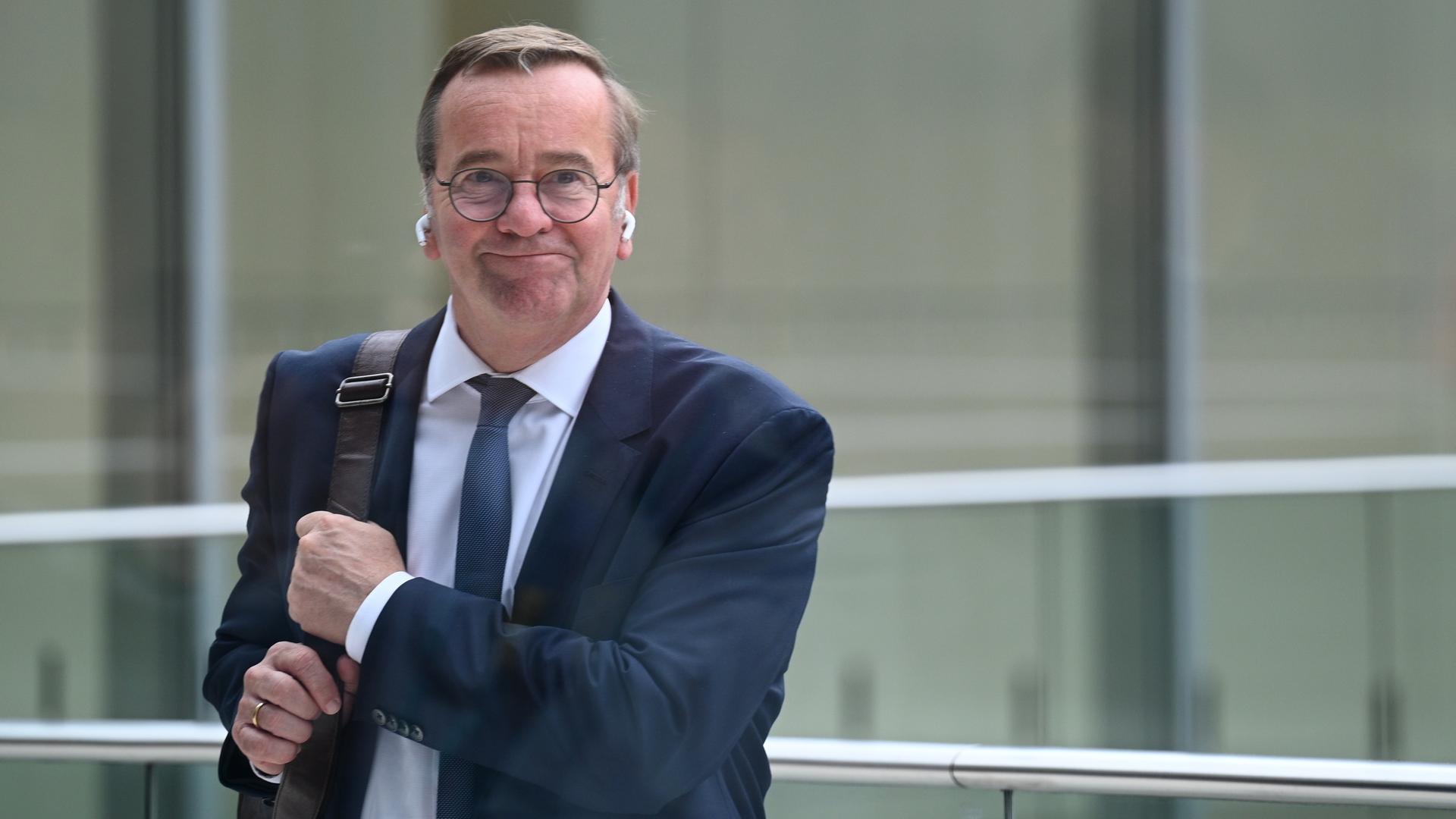 Boris Pistorius (SPD), Bundesverteidigungsminister, auf einer Terrasse des Reichstagsgebäudes; er trägt Anzug und Krawatte und hält mit beiden Händen eine Tasche, die über seiner Schulter hängt.