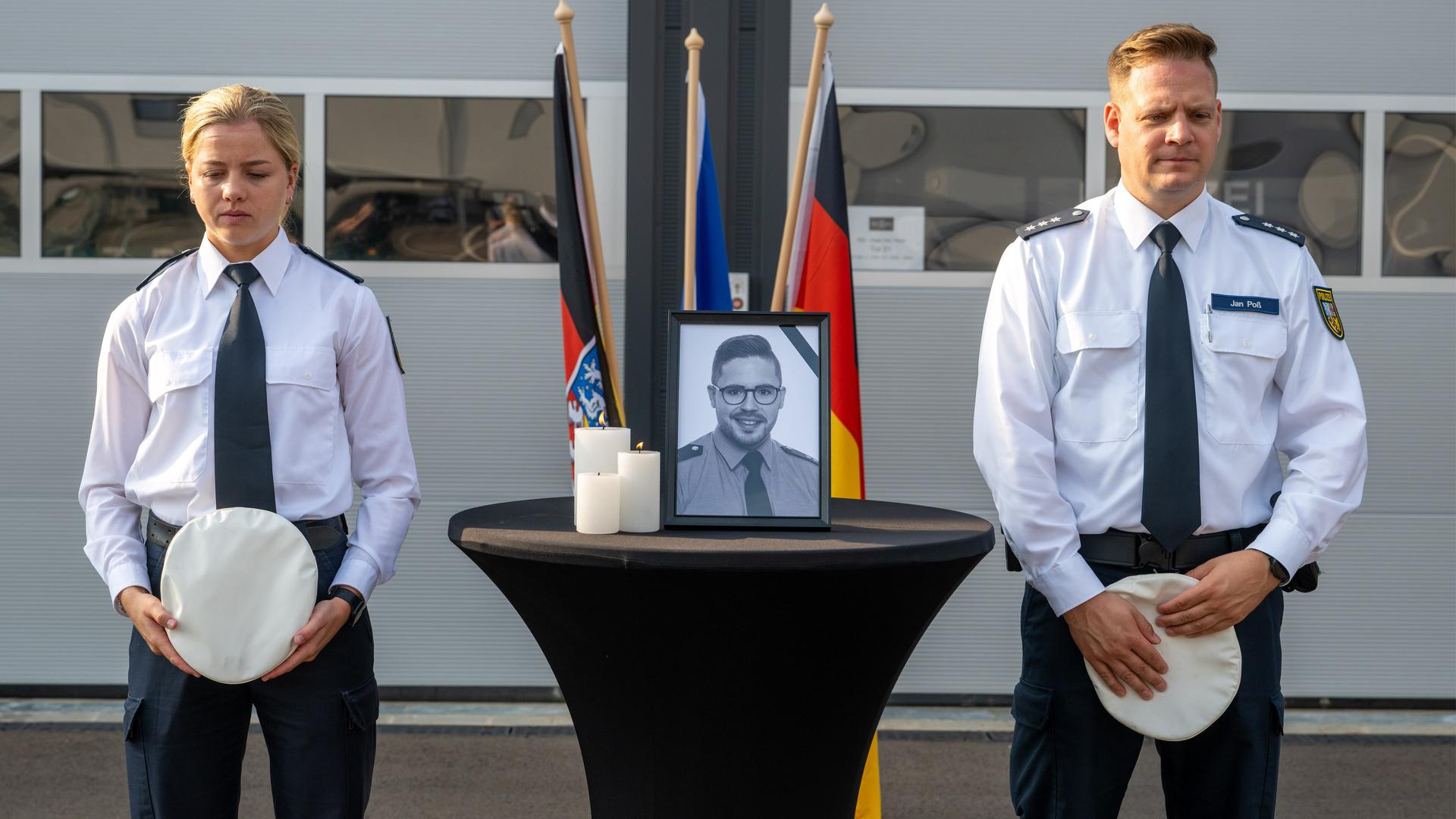 Polizeikommissarin Elisa Skrotzki (l) und Polizeioberkommissar Jan Poß stehen während einer Schweigeminute für den im Saarland getöteten Polizeioberkommissar neben dessen Portraitfoto. Polizeikommissarin Elisa Skrotzki (l) und Polizeioberkommissar Jan Poß stehen während einer Schweigeminute für den im Saarland getöteten Polizeioberkommissar neben dessen Portraitfoto.