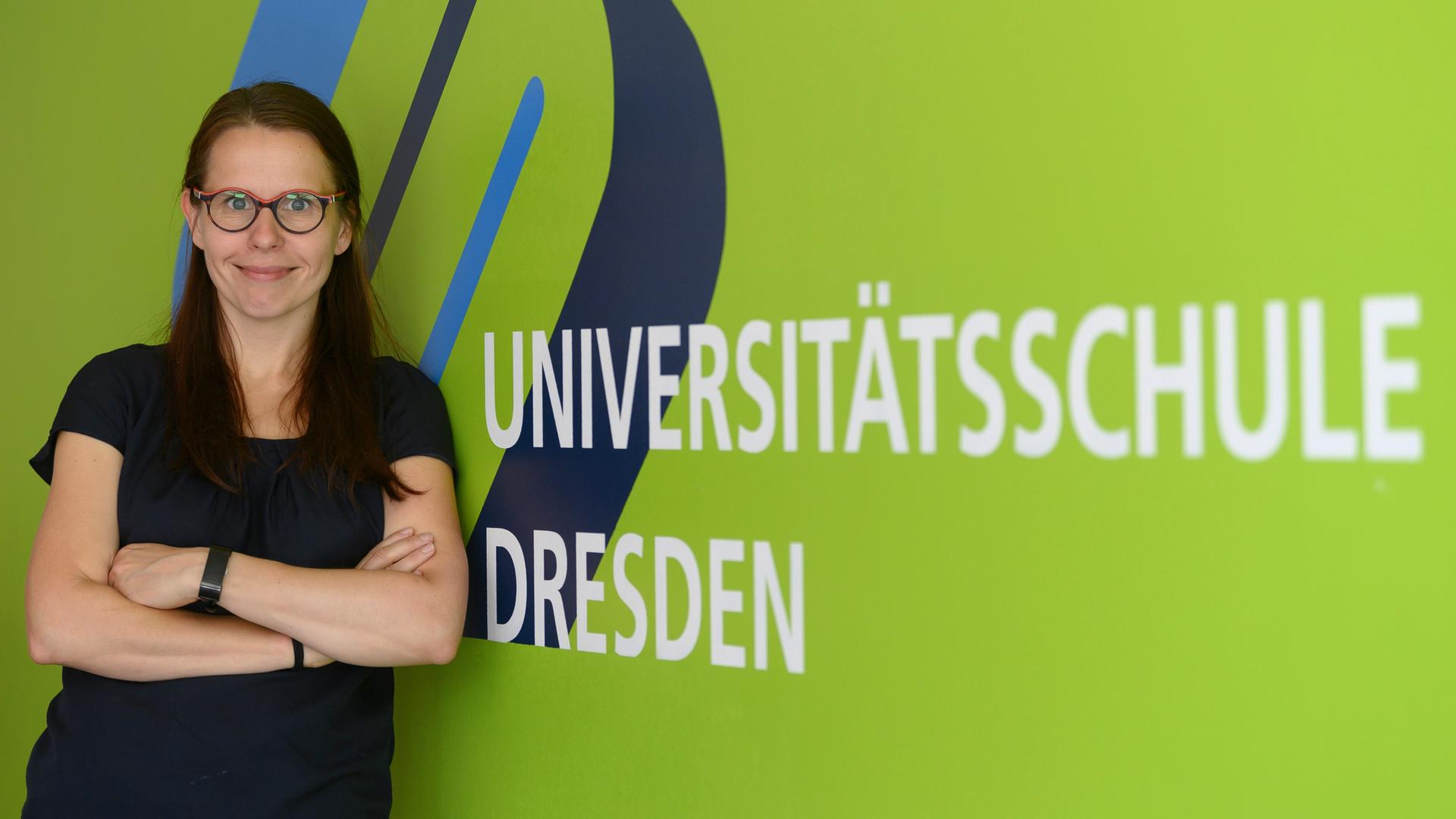 Anke Langner, wissenschaftliche Leiterin des Schulversuchs der Universitätsschule Dresden steht vor dem Logo der Schule.