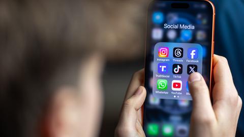 Ein Jugendlicher mit einem Smartphone auf dessen Display u.a. viele Social Media Anwendungen von Meta zu sehen sind. Der Hintergrund ist dunkel und verschwommen. Vom Jugendlichen ist nur ein Profil und die Hände zu sehen. Der Fokus ist auf dem Smarphone. Ein Jugendlicher mit einem Smartphone auf dessen Display u.a. viele Social Media Anwendungen von Meta zu sehen sind. Der Hintergrund ist dunkel und verschwommen. Vom Jugendlichen ist nur ein Profil und die Hände zu sehen. Der Fokus ist auf dem Smarphone.