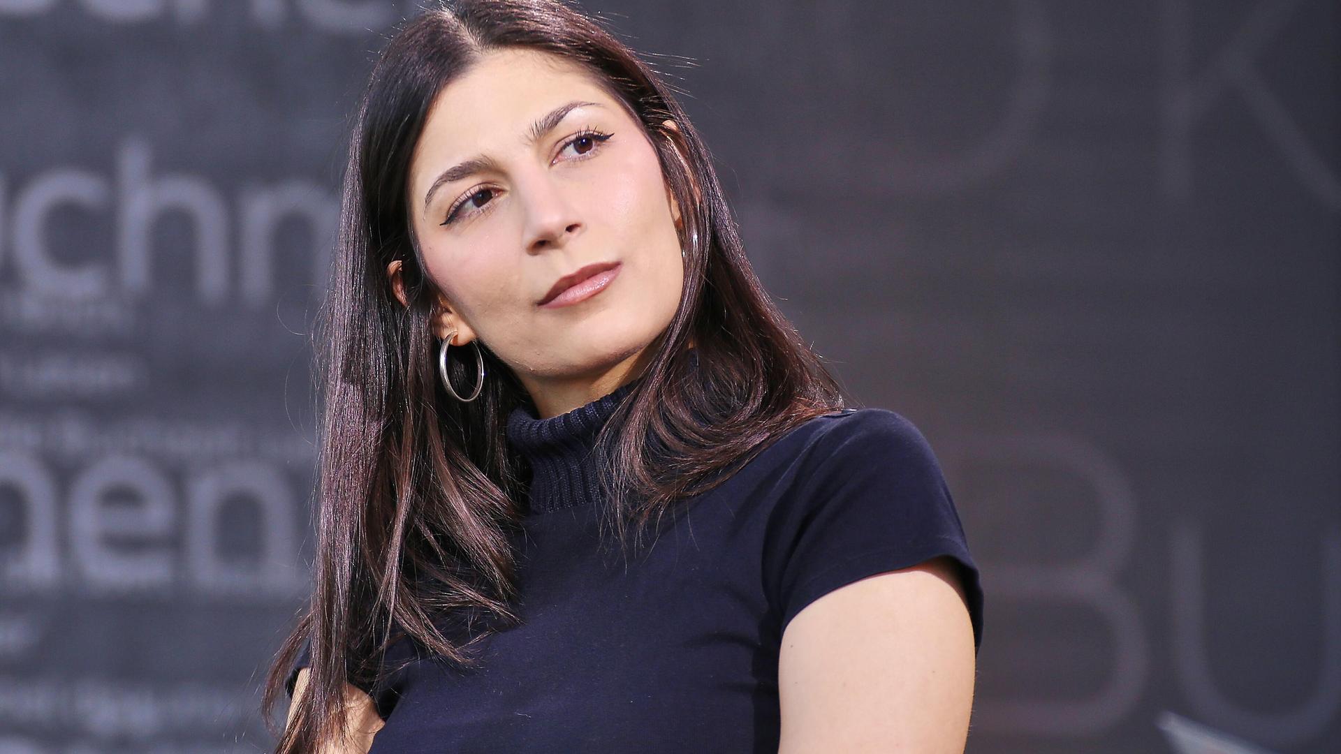 Miriam Davoudvandi trägt ein schwarzes Rollkragen-T-Shirt und hat den Kopf zur Seite geneigt.