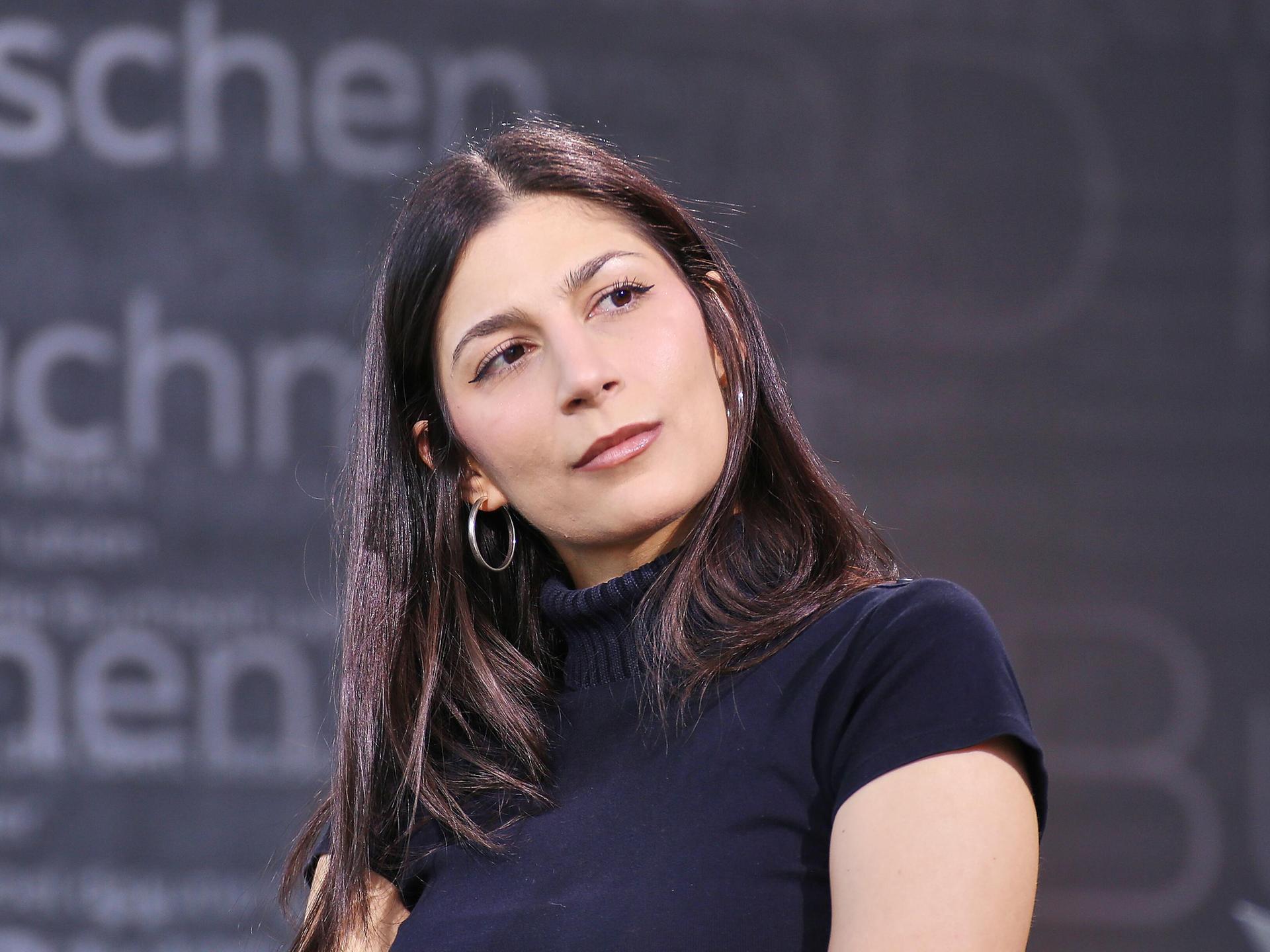Miriam Davoudvandi trägt ein schwarzes Rollkragen-T-Shirt und hat den Kopf zur Seite geneigt.