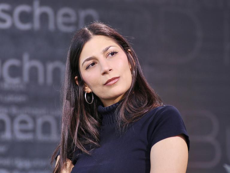 Miriam Davoudvandi trägt ein schwarzes Rollkragen-T-Shirt und hat den Kopf zur Seite geneigt.