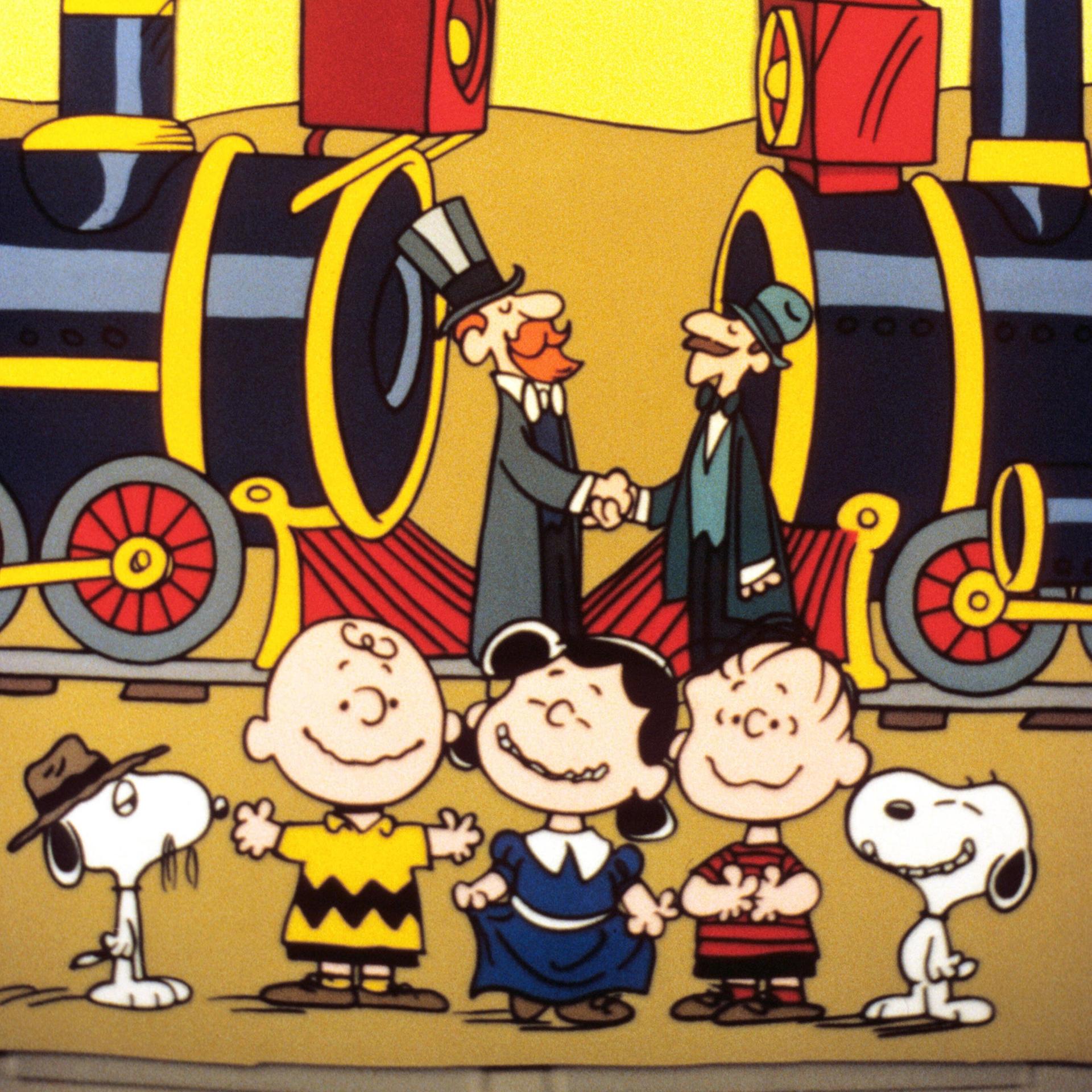 Ein Szenenfoto aus der Zeichentrickserie "The Building of the Transcontinental Railroad" mit den "Peanuts". Im Vordergrund des Bildes sind die "Peanuts"-Figuren Charlie Brown, Lucy und Linus sowie der Hund Snoopy zu sehen. 