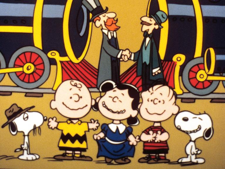 Ein Szenenfoto aus der Zeichentrickserie "The Building of the Transcontinental Railroad" mit den "Peanuts". Im Vordergrund des Bildes sind die "Peanuts"-Figuren Charlie Brown, Lucy und Linus sowie der Hund Snoopy zu sehen. 