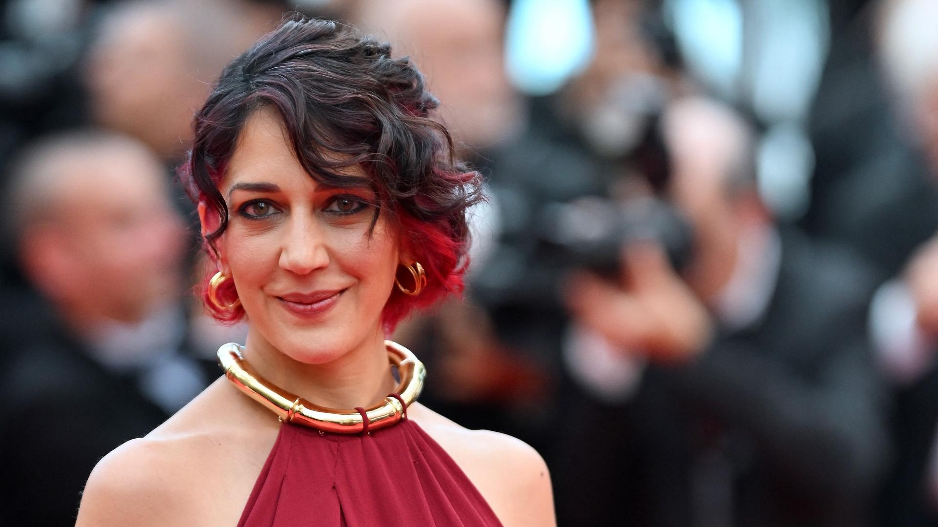 Zahra Amir Ebrahimi auf dem roten Teppich in Cannes in dunkelrotem Kleid und mit roten Stränen im schwarzen Haar Zahra Amir Ebrahimi auf dem roten Teppich in Cannes in dunkelrotem Kleid und mit roten Stränen im schwarzen Haar