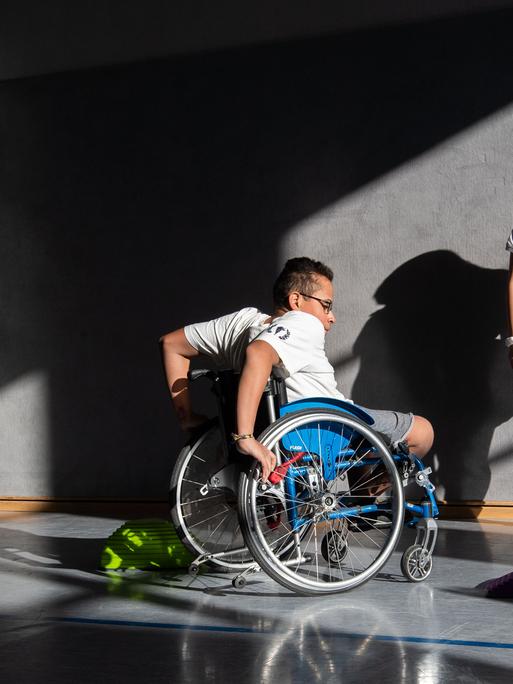 Ein Schüler der Förderschule Paul-Klee-Schule in Celle fährt mit seinem Rollstuhl in der Sporthalle des Gymnasium Burgdorf Slalom um Hindernisse, während eine Schülerin zuschaut.