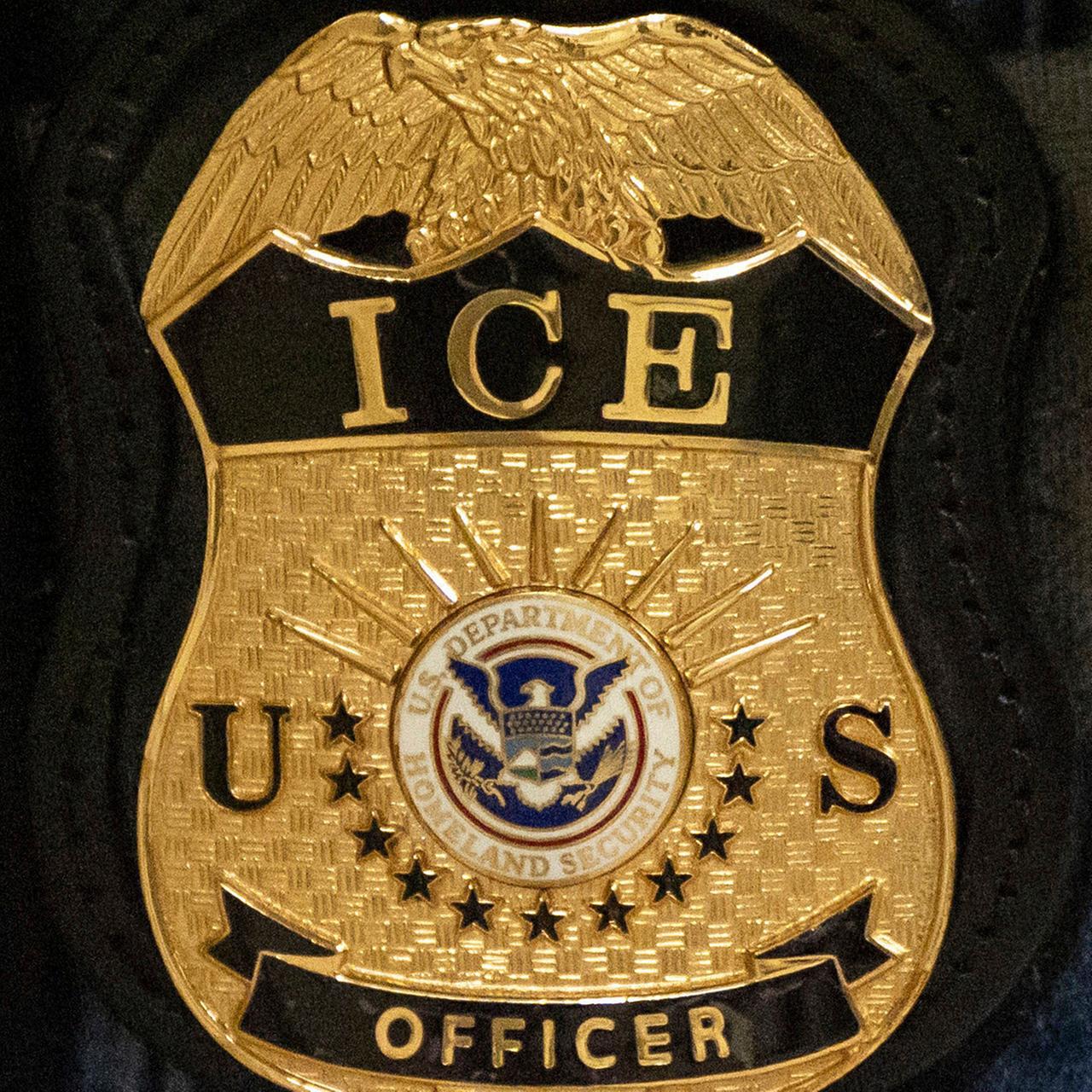 Nahaufnahme des goldenen Wappens auf dunkelblauem Stoff mit der Aufschrift "ICE US Officer" und einem integrierten US-Wappen 