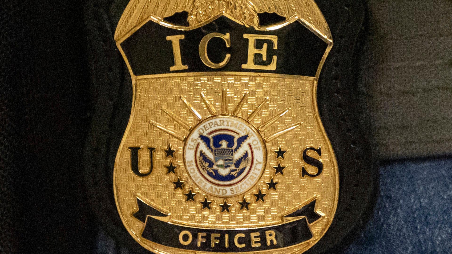 Nahaufnahme des goldenen Wappens auf dunkelblauem Stoff mit der Aufschrift "ICE US Officer" und einem integrierten US-Wappen 