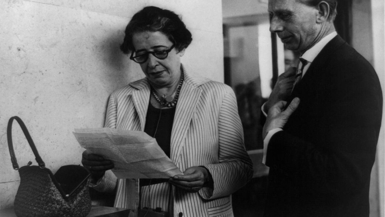 Schwarz-weiß Aufnahme von Hannah Arendt, die in einem Brief liest. Neben ihr steht ein Reporter.