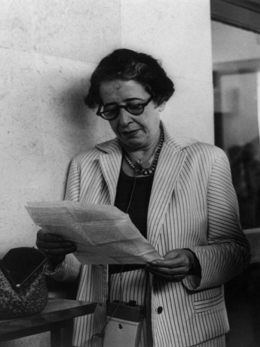 Schwarz-weiß Aufnahme von Hannah Arendt, die in einem Brief liest. Neben ihr steht ein Reporter.