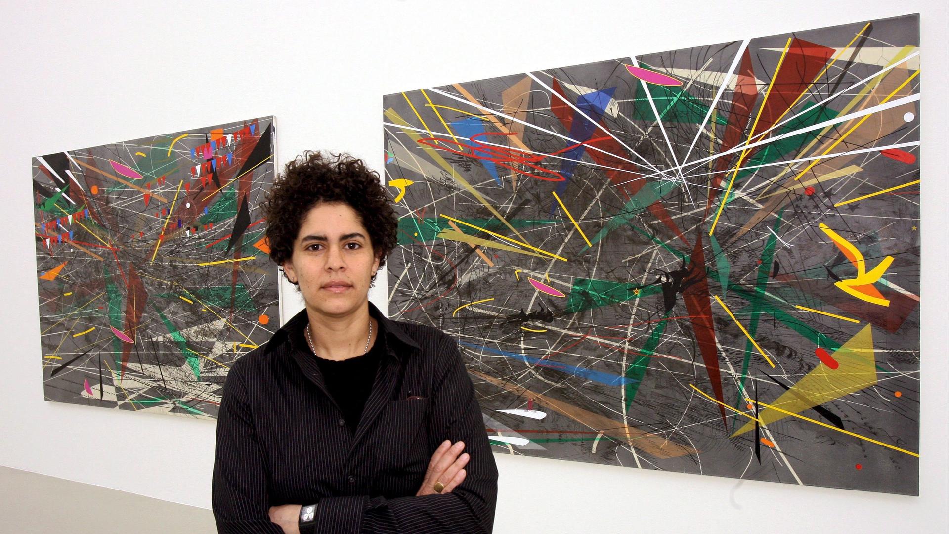 Die Künstlerin Julie Mehretu steht mit verschränkten Armen vor zwei ihrer farbigen Arbeiten Die Künstlerin Julie Mehretu steht mit verschränkten Armen vor zwei ihrer farbigen Arbeiten