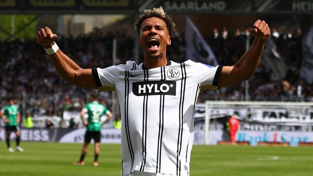 Der Spieler Bambase Conte von der SV Elversberg hat beide Arme erhoben, die Hände sind zu Fäusten geballt.