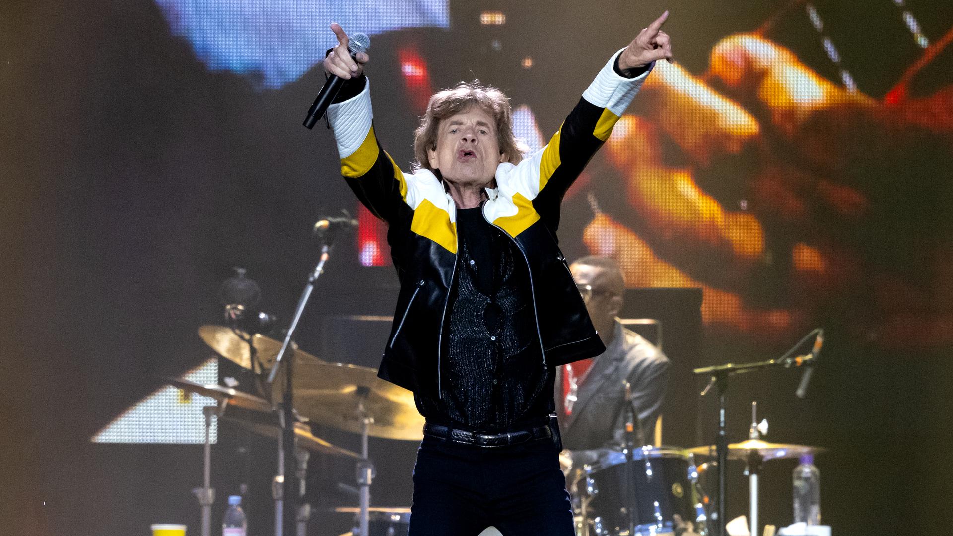Mick Jagger zeigt mit beiden Zeigefingern nach oben.