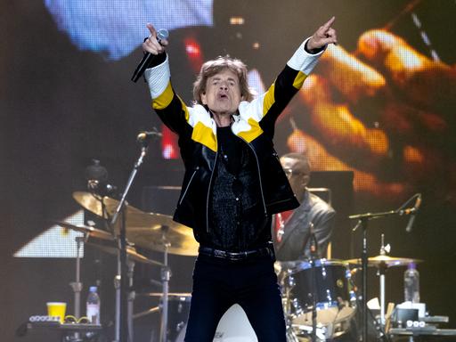 Mick Jagger zeigt mit beiden Zeigefingern nach oben.