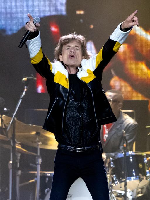 Mick Jagger zeigt mit beiden Zeigefingern nach oben.