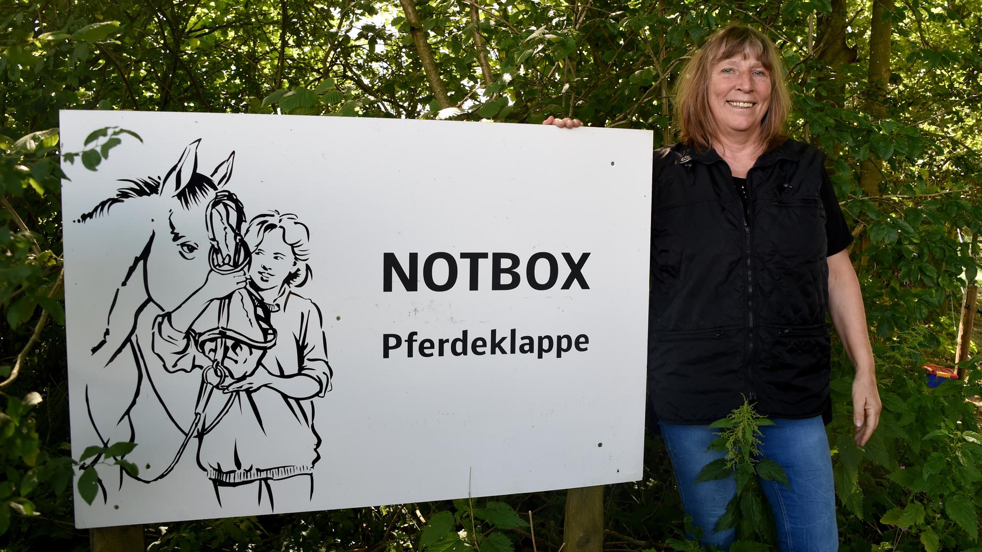 Pferdeklappe-Chefin Petra Teegen steht in Norderbrarup vor einem Schild mit der Aufschrift Notbox.