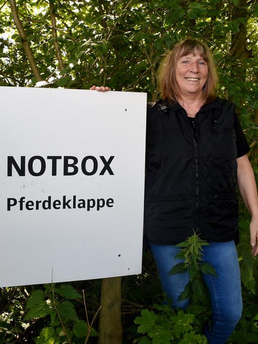 Pferdeklappe-Chefin Petra Teegen steht in Norderbrarup vor einem Schild mit der Aufschrift Notbox.