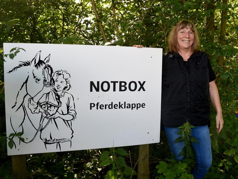 Pferdeklappe-Chefin Petra Teegen steht in Norderbrarup vor einem Schild mit der Aufschrift Notbox.