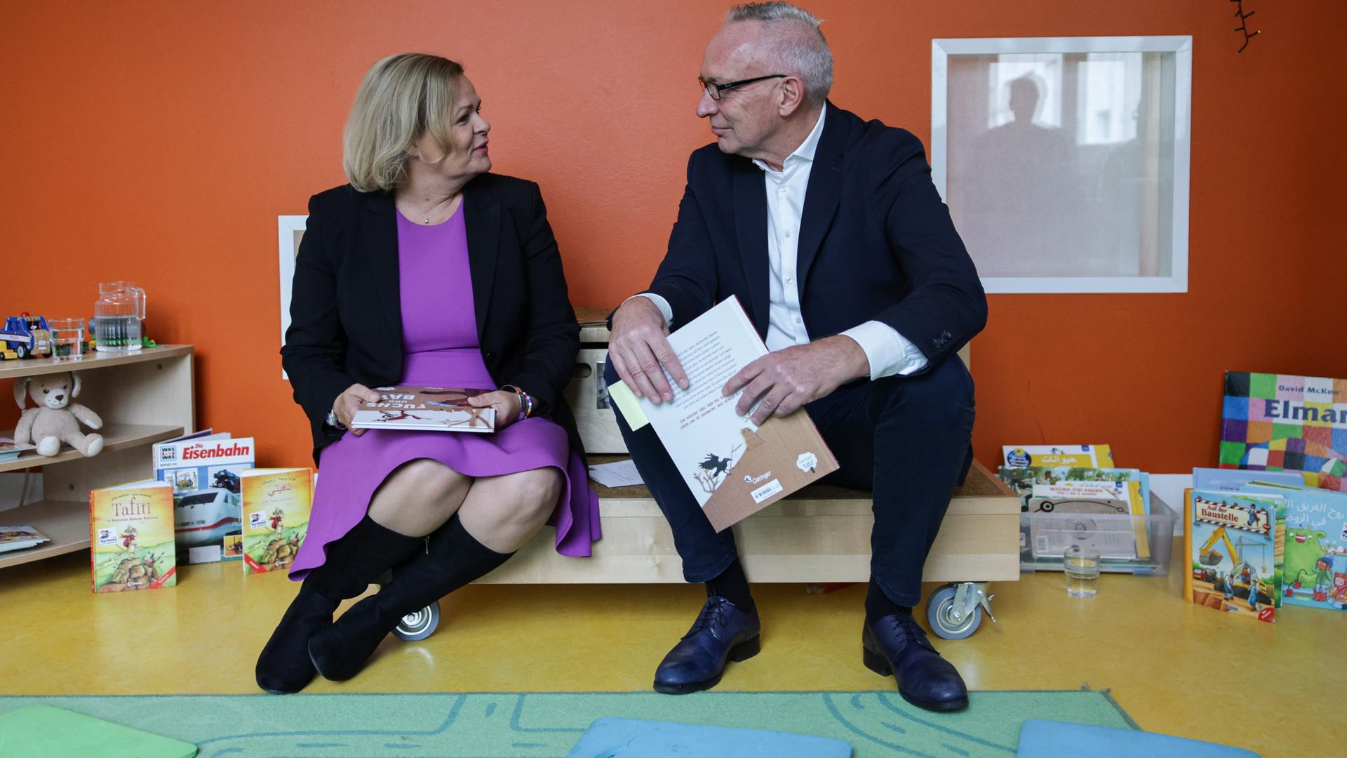 Bundesinnenministerin Faeser und der Hauptgeschäftsführer der Stiftung Lesen, Jörg Maas, sitzen in einer Kita auf einem Rollwagen und Lesen aus Büchern vor.