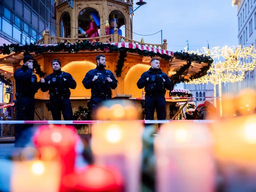 Polizisten sichern den Weihnachtsmarkt, wobei Kerzen vor ihnen brennen.