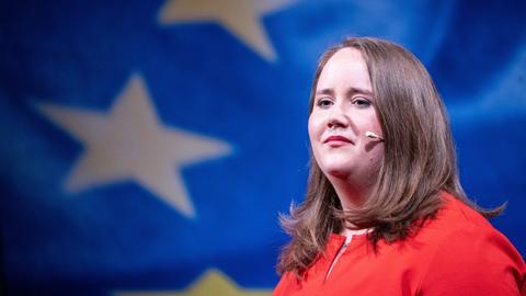 Ricarda Lang mit rotem Oberteil vor blauem Hintergrund mit gelben Europasternen.