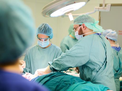 Eine Operation im Unfallkrankenhaus Berlin. Menschen in grünen Kitteln mit OP-Masken stehen um einen Patienten herum. 