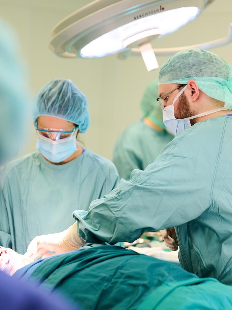Eine Operation im Unfallkrankenhaus Berlin. Menschen in grünen Kitteln mit OP-Masken stehen um einen Patienten herum. 