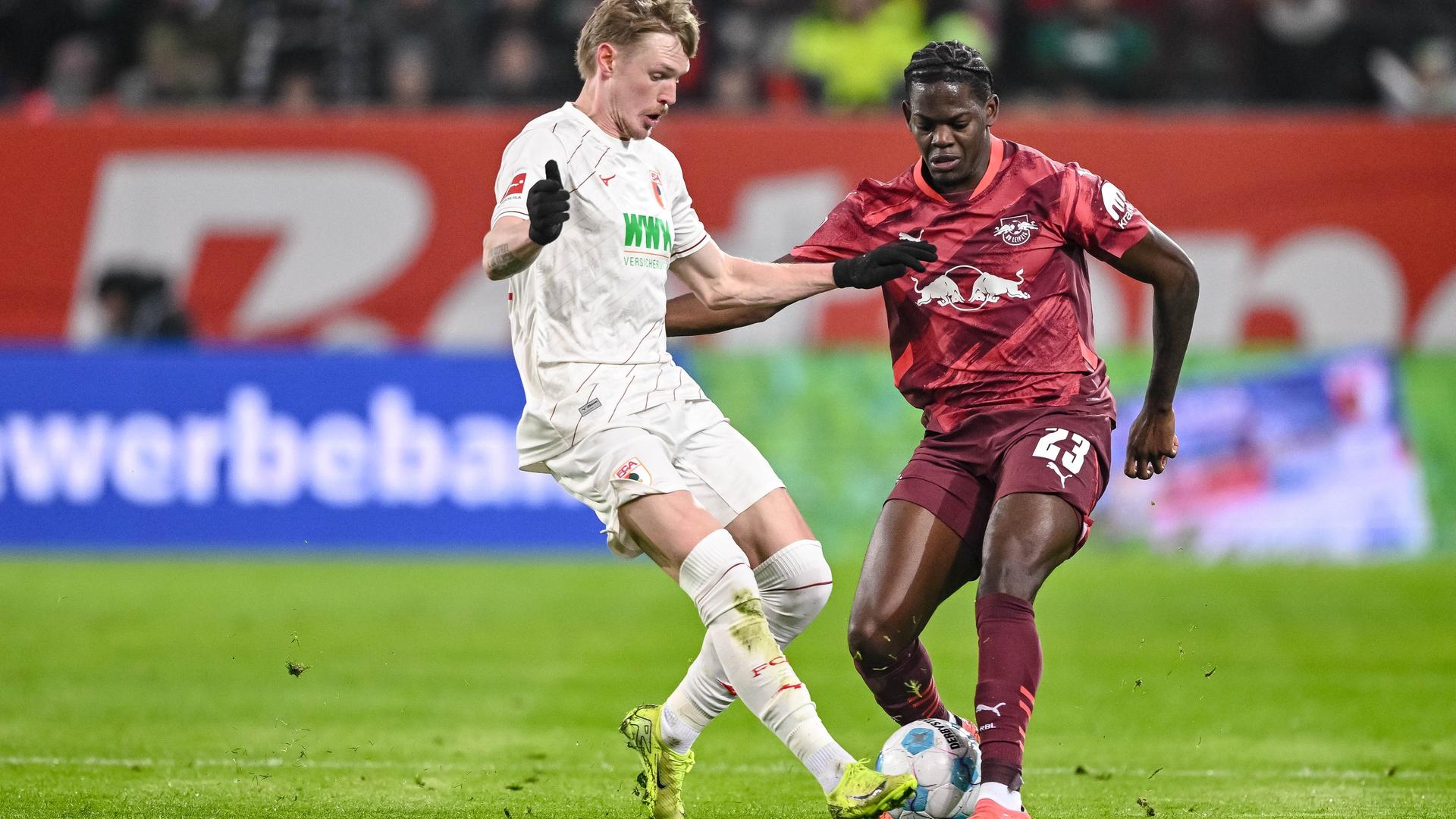 Das Foto zeigt Augsburgs Spieler Fredrik Jensen (links) in Aktion mit Leipzigs Castello Lukeba.