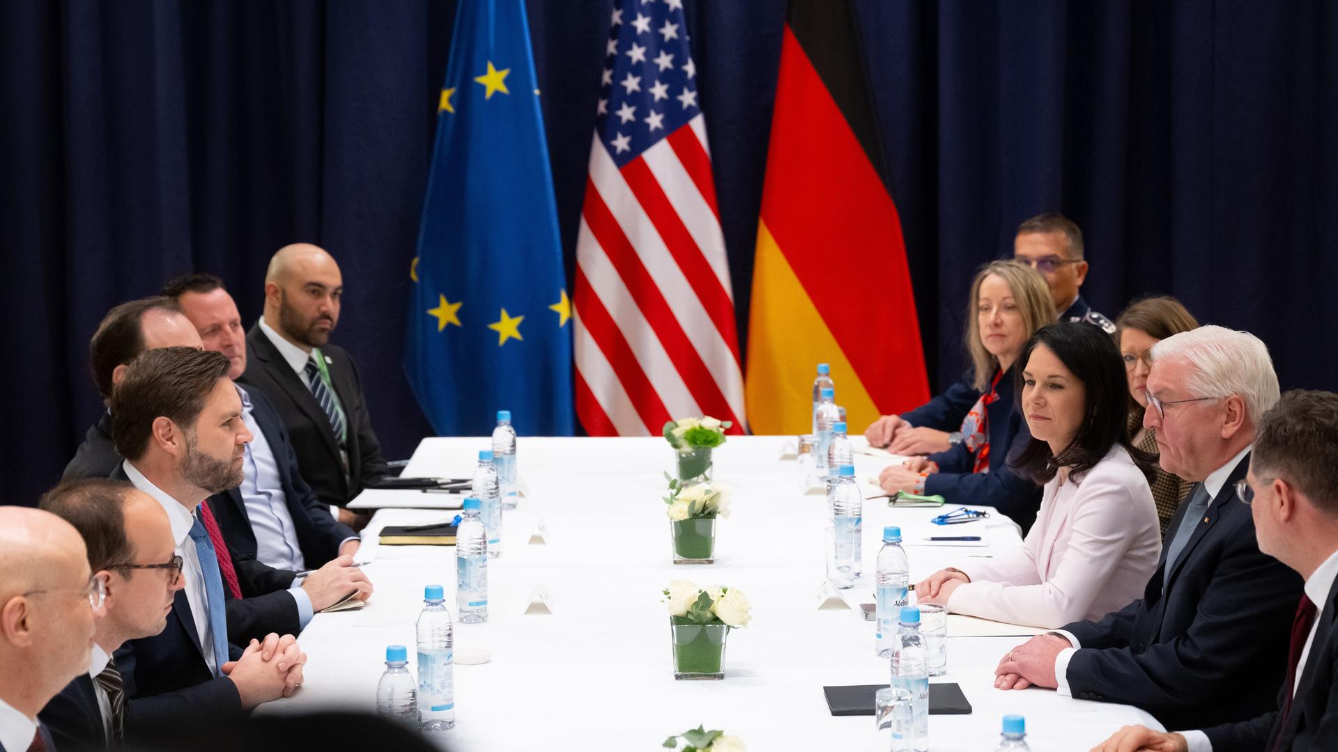 Mehrere Politiker, darunter Bundespräsident Frank-Walter Steinmeier, Bundesaußenministerin Annalena Baerbock und US-Vizepräsident J. D. Vance an einem Konferenztisch, dahinter die Flaggen der EU, der USA und Deutschlands.