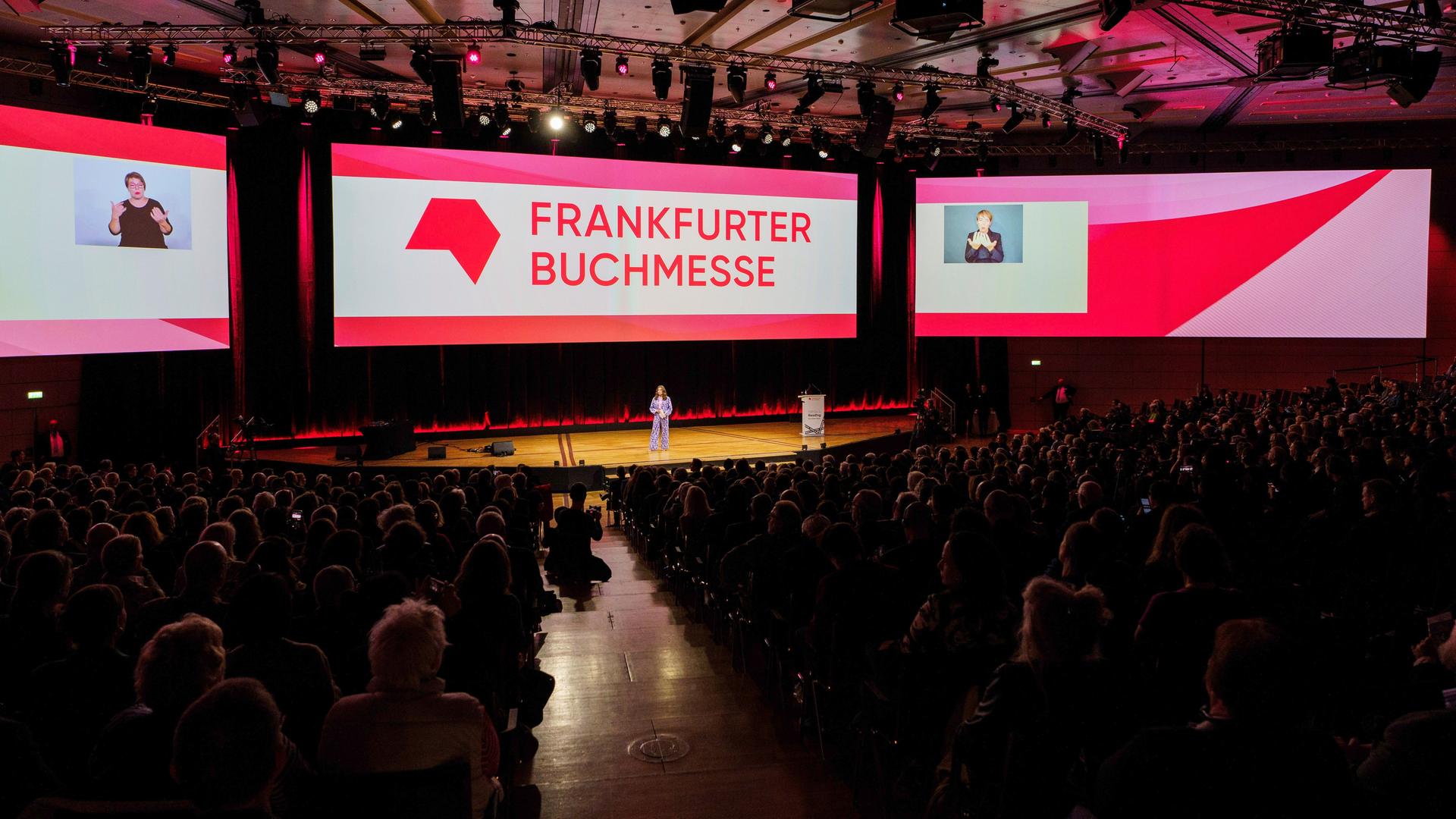 Frankfurt/Main: Mit einer Feier wird die 76. Frankfurter Buchmesse (16. - 20. Oktober 2024) offiziell eröffnet. Bildschirme mit dem Schriftzug Frankfurter Buchmesse, vor denen Menschen im Podium sitzen.