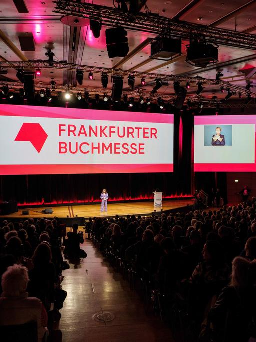 Frankfurt/Main: Mit einer Feier wird die 76. Frankfurter Buchmesse (16. - 20. Oktober 2024) offiziell eröffnet. Bildschirme mit dem Schriftzug Frankfurter Buchmesse, vor denen Menschen im Podium sitzen.