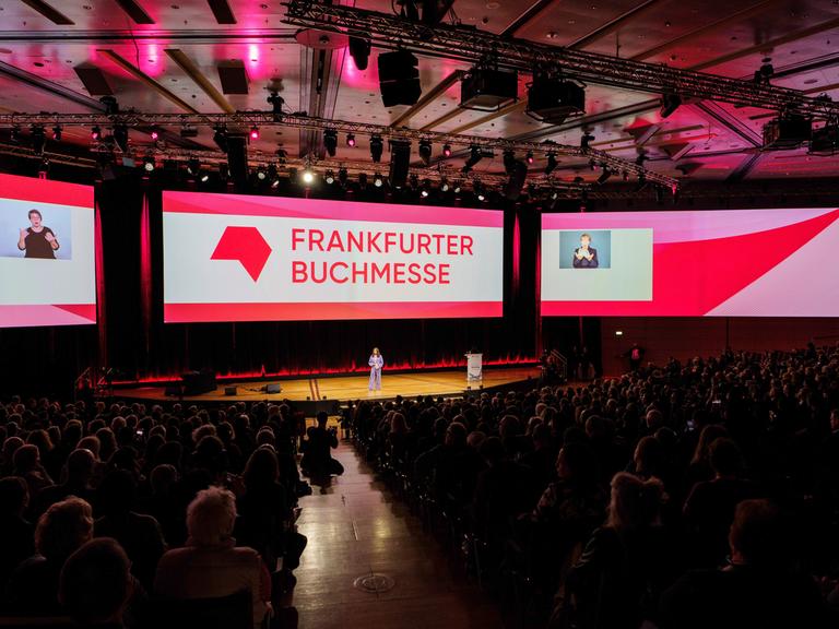 Frankfurt/Main: Mit einer Feier wird die 76. Frankfurter Buchmesse (16. - 20. Oktober 2024) offiziell eröffnet. Bildschirme mit dem Schriftzug Frankfurter Buchmesse, vor denen Menschen im Podium sitzen.