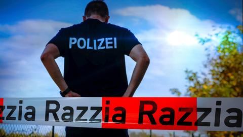 Ein Polizist steht vor blauem Himmel mit dem Rücken zur Kamera. Davor Absperrband mit der Aufschrift Razzia.