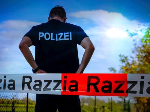 Ein Polizist steht vor blauem Himmel mit dem Rücken zur Kamera. Davor Absperrband mit der Aufschrift Razzia.