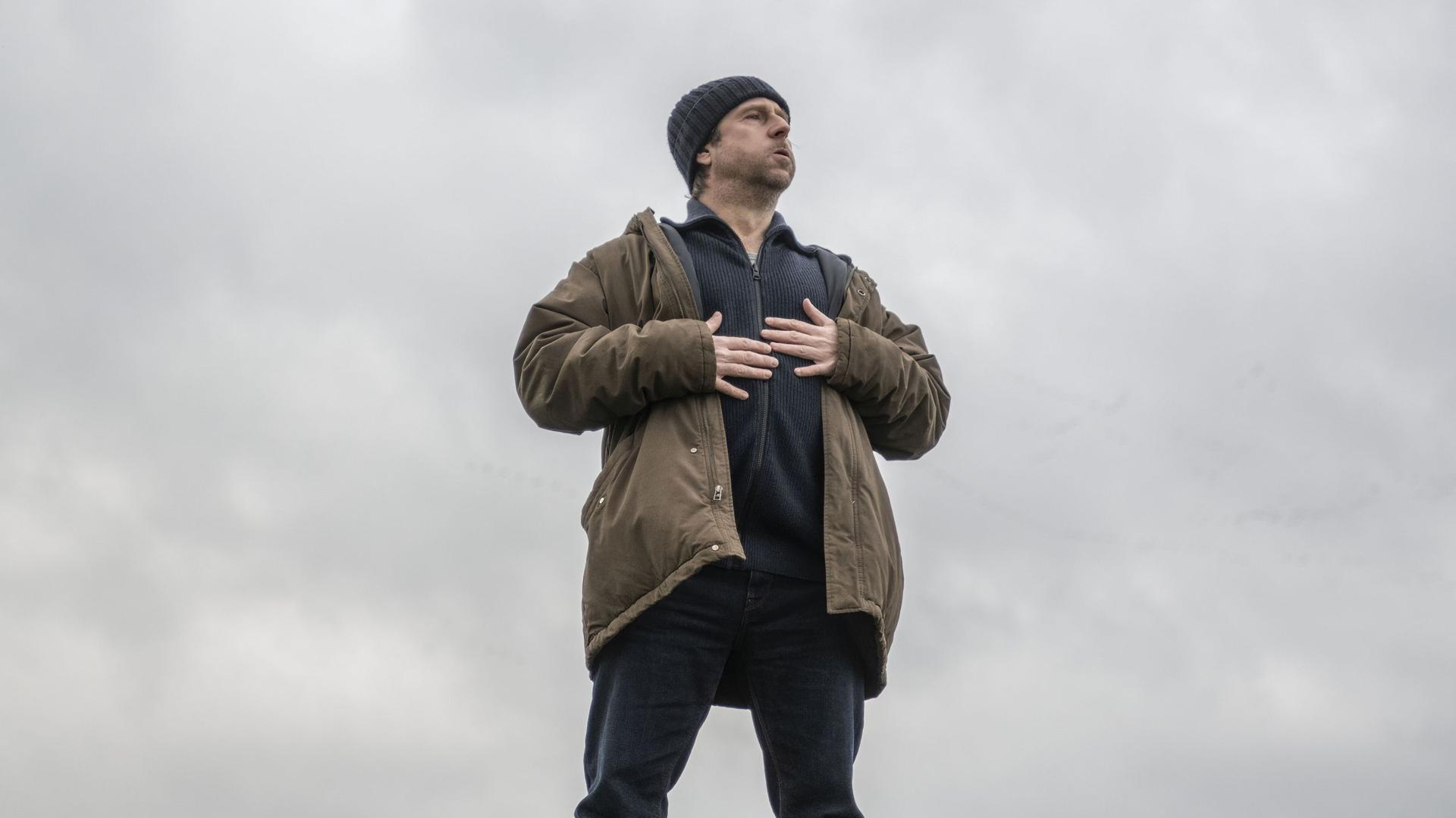 Bjarne Mädel als Kommissar Sörensen steht auf einem Deich, blickt nach oben und hält die Hände auf die Brust.