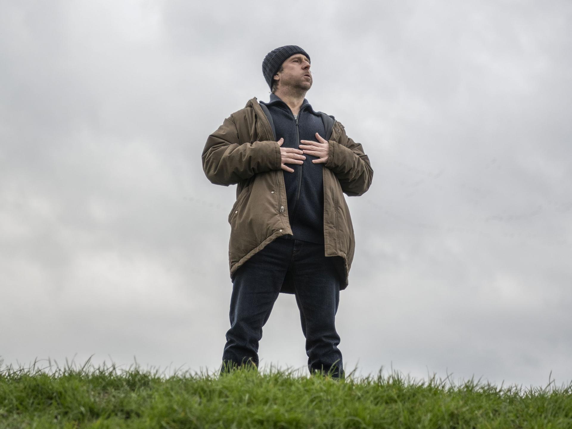 Bjarne Mädel als Kommissar Sörensen steht auf einem Deich, blickt nach oben und hält die Hände auf die Brust.