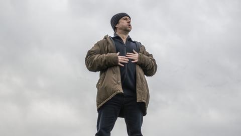 Bjarne Mädel als Kommissar Sörensen steht auf einem Deich, blickt nach oben und hält die Hände auf die Brust.