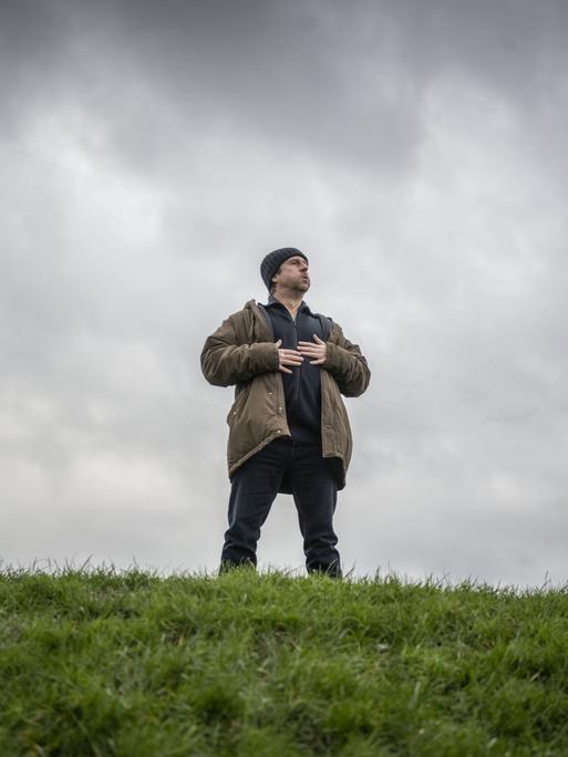 Bjarne Mädel als Kommissar Sörensen steht auf einem Deich, blickt nach oben und hält die Hände auf die Brust.