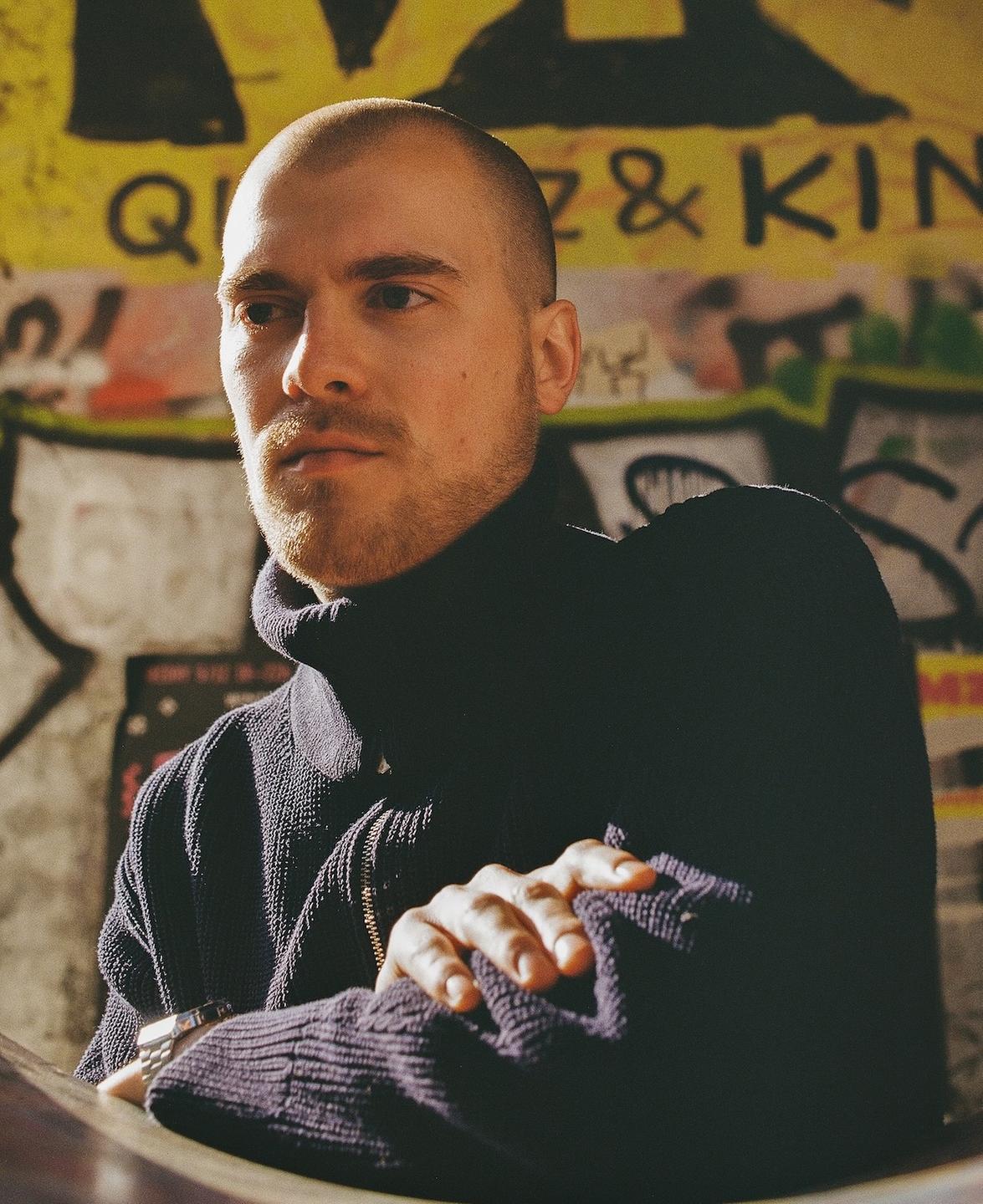 Porträt von Ulrich Krischtan in schwarzem Rollkragenpullover vor einer Wand mit Grafitti. Porträt von Ulrich Krischtan in schwarzem Rollkragenpullover vor einer Wand mit Grafitti.