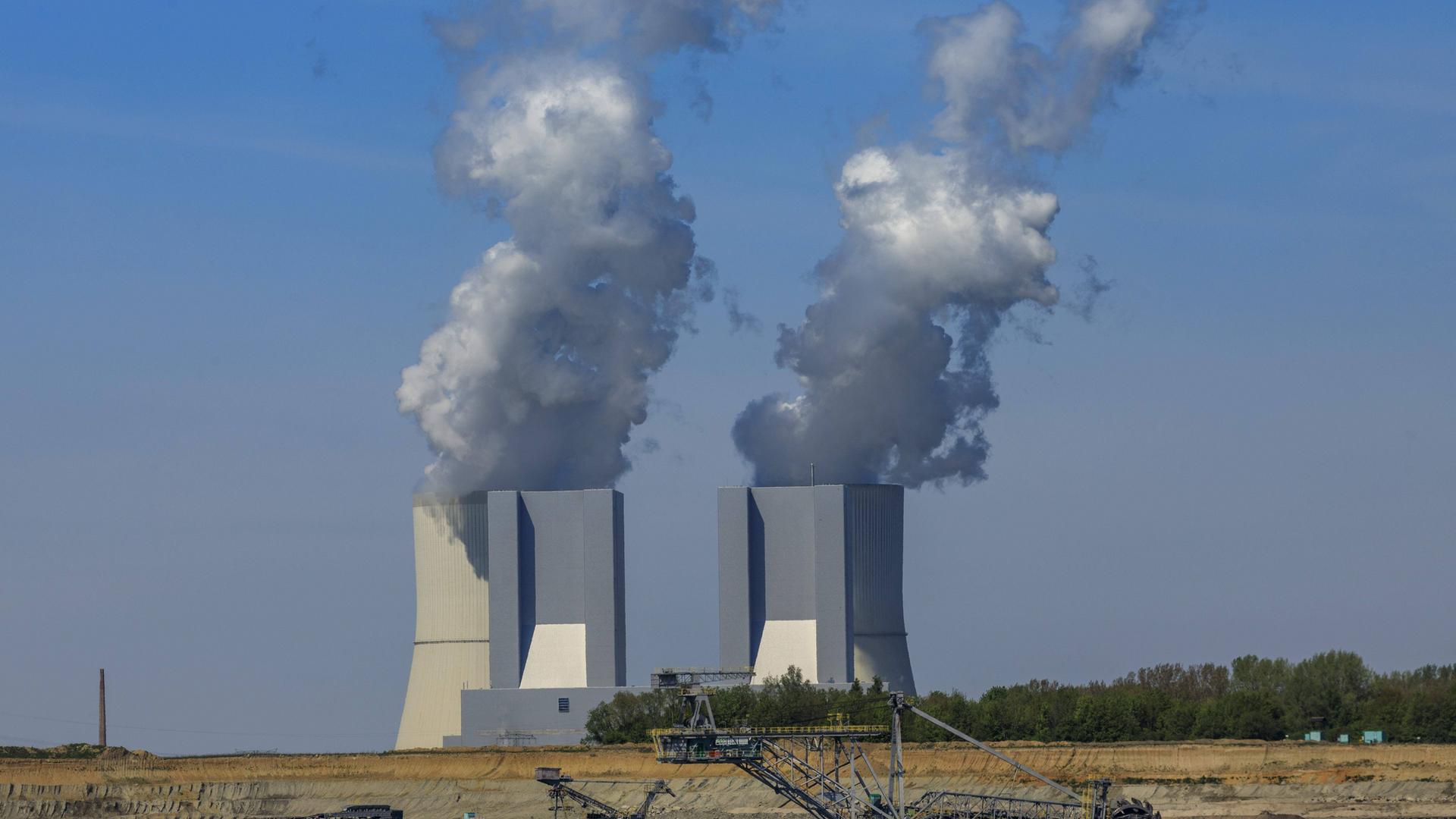 Im Vordergrund steht ein Bagger zum Abbau von Kohle. Weiter hinten sind rauchende Schlote und ein Kohlekraftwerk.