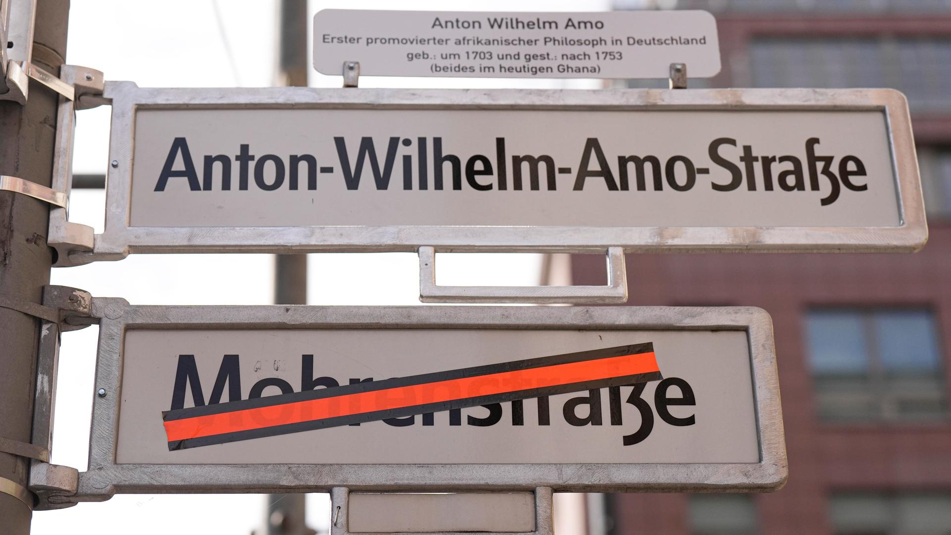 Zu sehen sind zwei Straßenschilder. Oben steht Anton-Wilhelm-Amo-Straße, darunter Mohrenstraße. Dieser Name ist mit einem roten Klebeband überklebt. Zu sehen sind zwei Straßenschilder. Oben steht Anton-Wilhelm-Amo-Straße, darunter Mohrenstraße. Dieser Name ist mit einem roten Klebeband überklebt.