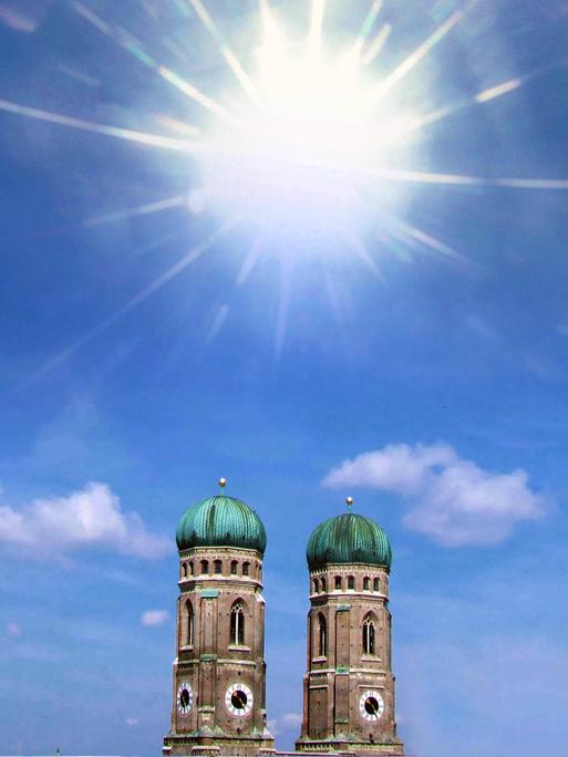 Die Türme der Frauenkirche in München vor blauem Himmel und viel Sonnenschein. Es wirkt sehr heiß.
