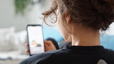 Eine Frau liegt auf einem Sofa und schaut sich ein Video auf der Social-Media-Plattform Instagram auf ihrem Handy an. 