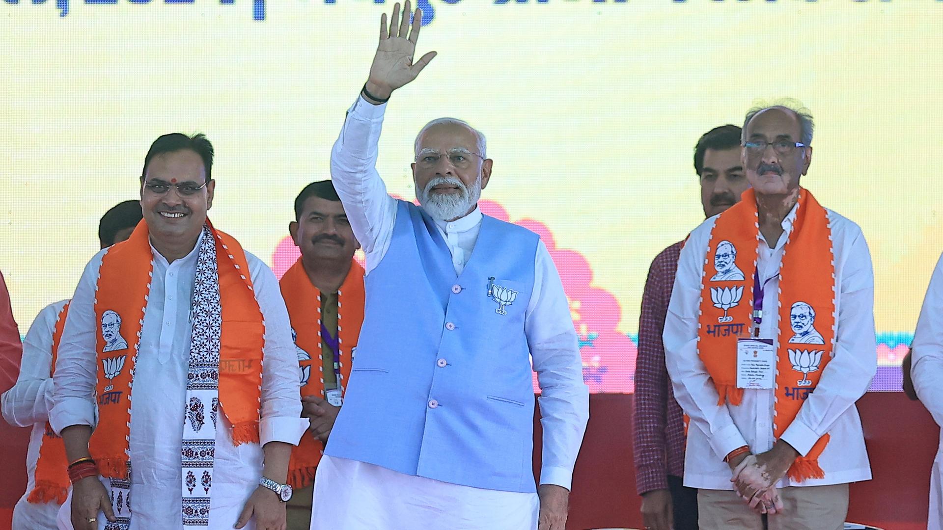 Der indische Premierministers Narendra Modi steht auf einer Bühne. Er hat eine Hand zum Gruß erhoben. 