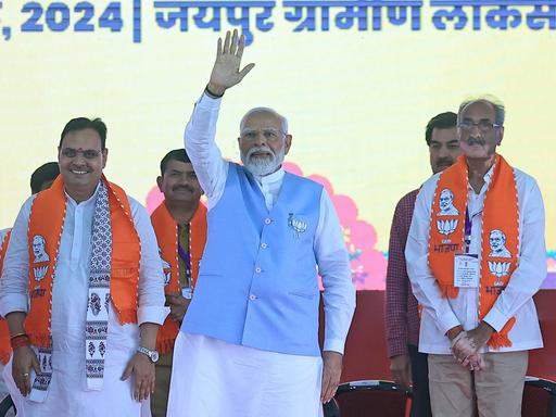 Der indische Premierministers Narendra Modi steht auf einer Bühne. Er hat eine Hand zum Gruß erhoben. 