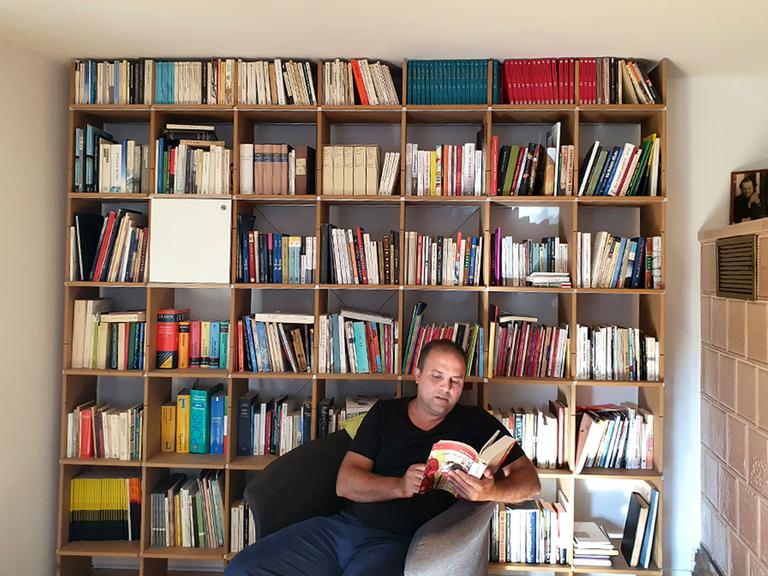 Der jemenitische Dichter Osama Al-Dhari sitzt vor einem Bücherregel und blätter in einem Buch. 