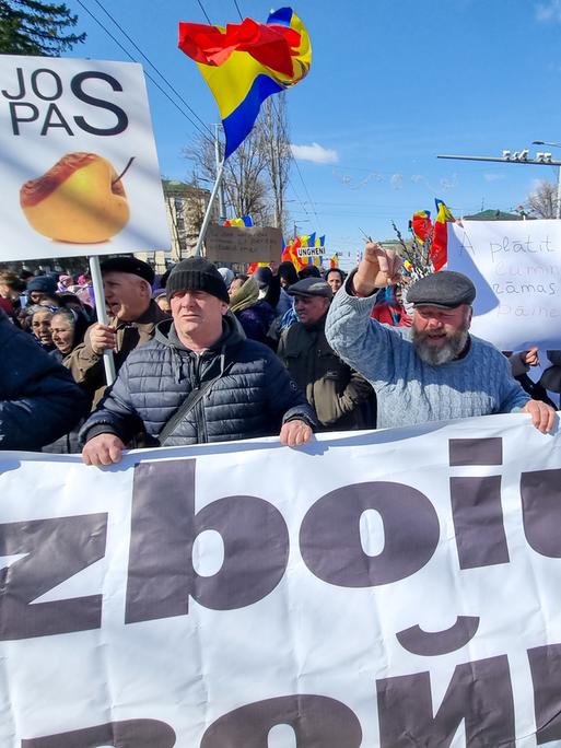 Demonstranten laufen über eine Straße. Sie halten ein Banner und schwenken die moldawische Fahne.