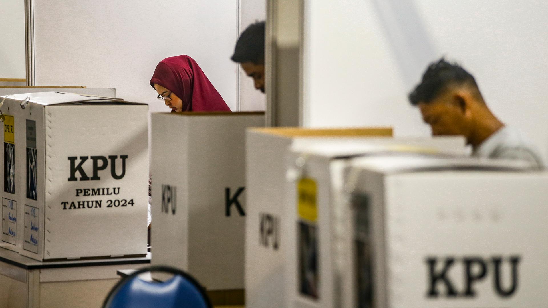 Menschen stehen hinter mehreren Wahlurnen, auf denen das Kürzel der indonesischen Wahlkommission KPU prangt. Menschen stehen hinter mehreren Wahlurnen, auf denen das Kürzel der indonesischen Wahlkommission KPU prangt.