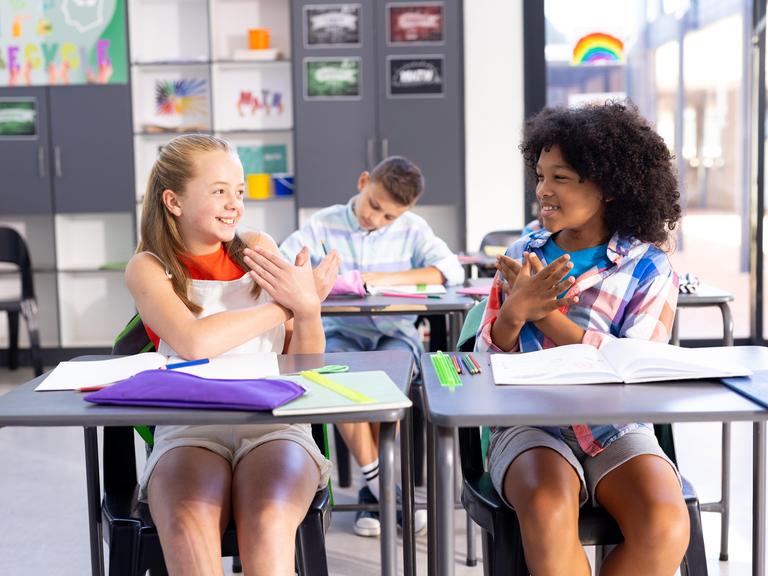 Zwei lächelnde Mädchen unterhalten sich im Klassenraum in Gebärdensprache